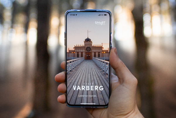 en hand som håller en smartphone med en bild på Visit Varbergs app